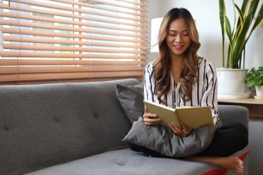Rahatlamış milenyum kadını evde kanepede dinlenirken kitap okuyor..