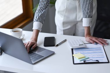 Tanımlanamayan iş kadını hesap makinesi kullanıyor ve ofis masasında dizüstü bilgisayarla çalışıyor..