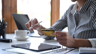 Kredi kartı tutan ve dijital tablette online bankacılık yapan genç bir kadın..