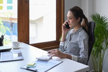 Çekici bayan girişimci cep telefonuyla konuşuyor ve pencereden bakıyor..
