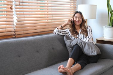 Çekici milenyum kadını evdeki kanepede dinleniyor ve cep telefonuyla konuşuyor..