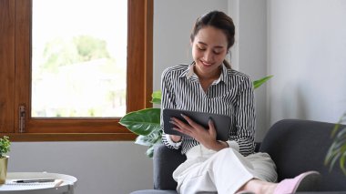 Rahatlamış genç bir kadın hafta sonunun tadını çıkarıyor ve dijital tablette internette sörf yapıyor..