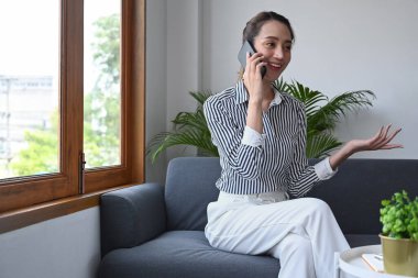 Parlak oturma odasında oturan ve cep telefonuyla konuşan güzel bir bayan..