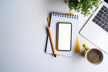 Akıllı telefon, dizüstü bilgisayar, not defteri ve kahve fincanı beyaz ofis masasının üzerinde duruyordu..