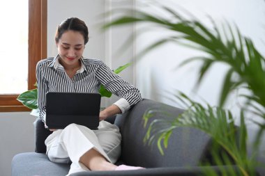 Rahat koltukta oturan ve dijital tablet kullanan hoş bir genç kadın..