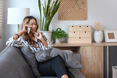 Güzel bir milenyum kadını evdeki koltukta dinleniyor ve cep telefonuyla konuşuyor..