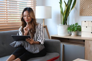 İnternette sörf yapan neşeli genç bir kadın dijital tabletten alışveriş yapıyor..