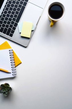 Laptop bilgisayarı, kahve fincanı, defter ve beyaz masadaki yapışkan notla basit bir iş yeri..