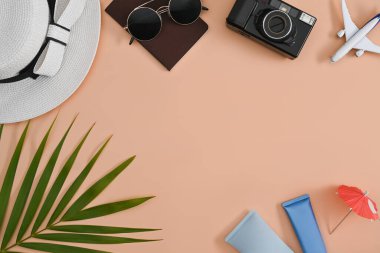 Geçmişe dönük kamerası, güneş gözlüğü, güneş kremi şişesi ve bej arka planda pasaportu olan gezgin aksesuarları. Seyahat, yaz ve tatil konsepti.