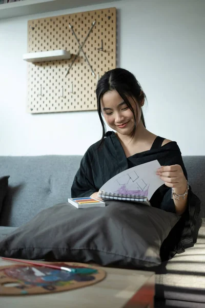 Feliz Ásia Menina Desenho Algo Ela Notebook Enquanto Sentado Sofá — Fotografia de Stock