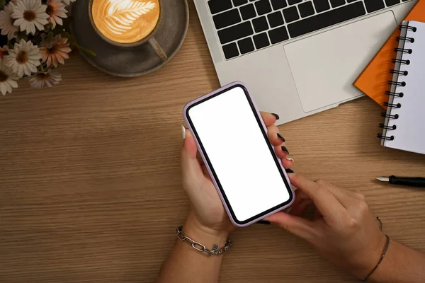 İş yerinde dizüstü bilgisayarın önünde oturan ve cep telefonu kullanan genç bir kadın..