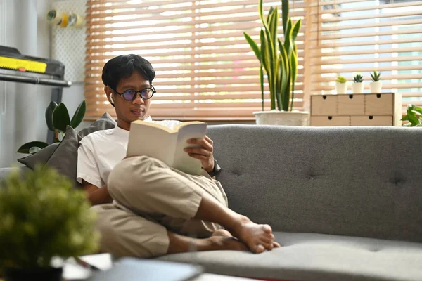 Χαλαρός Ασιάτης Κάθεται Στον Καναπέ Στο Σπίτι Και Διαβάζει Βιβλία — Φωτογραφία Αρχείου