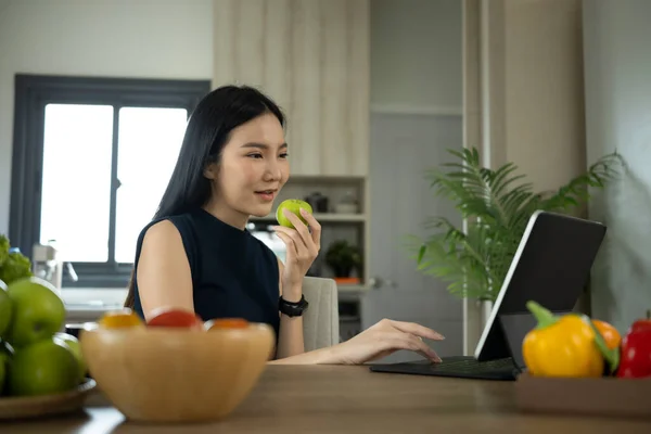 Ελκυστική Γυναίκα Τρώει Μήλο Και Χρήση Tablet Υπολογιστή Στην Κουζίνα — Φωτογραφία Αρχείου
