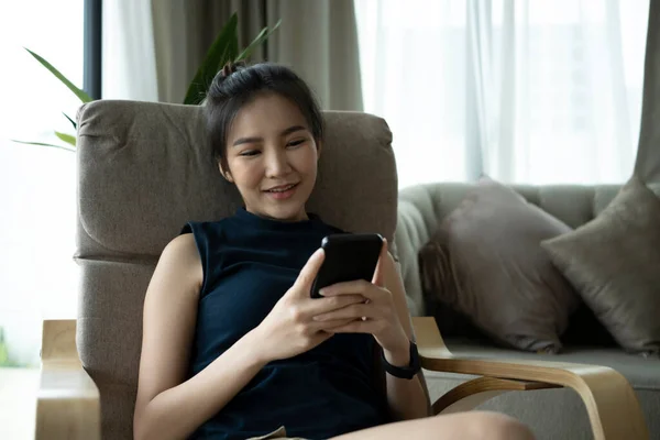 밀레니엄 여성은 거실에 앉아서 스마트폰으로 미디어를 합니다 — 스톡 사진
