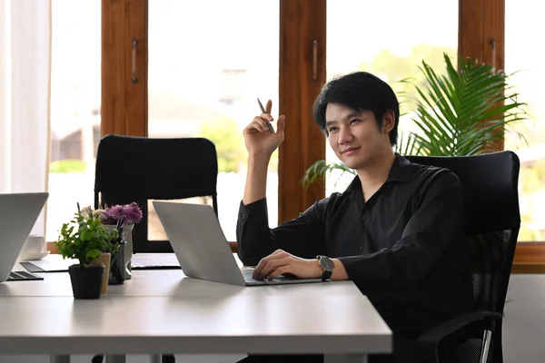 Χαμογελαστός Νεαρός Ασιάτης Επιχειρηματίας Που Κάθεται Στο Γραφείο Και Χρησιμοποιεί — Φωτογραφία Αρχείου