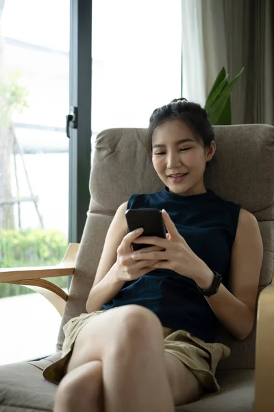 거실에 앉아서 스마트폰으로 미디어를 확인하는 만족하는 아시아 — 스톡 사진