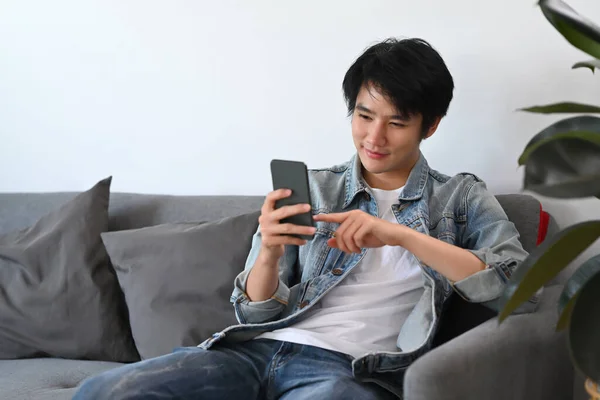 穿着休闲装的快乐男人使用智能手机 查看社交媒体 在沙发上放松地点菜 — 图库照片