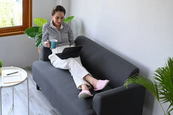 Kanepede oturup bilgisayar tableti kullanan, sosyal medyada vakit geçiren sıradan bir genç kadın..