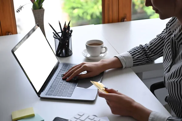 Kredi kartı tutan ve dizüstü bilgisayarda internet bankacılığı hizmetini kullanan bir kadın görüntüsü.