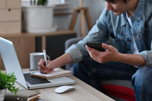 Sorridente Asiatico Uomo Holding Cellulare Making Notes Notebook Mentre Lavoro — Foto Stock