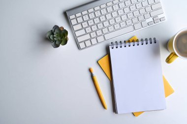 Boş defter, kablosuz klavye ve kahve fincanı beyaz ofis masasında..