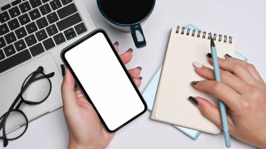 Cep telefonu kullanan ve beyaz ofis masasında çalışan kadın tasarımcı.