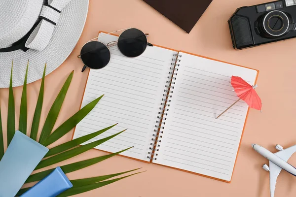 Not defteri, güneş gözlüğü, kamera ve bej arka planda şapkası olan gezgin aksesuarları. Yaz tatili kavramı.