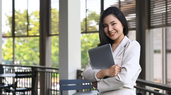 Pretty young female employee holding laptop and smiling to camera while standing on a terrace outside office — Stock Photo, Image