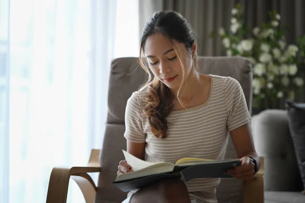 Peaceful millennial woman relaxing on armchair and reading book.