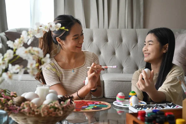 Positive mother and daughter painting Easter eggs together in living room. — Stock fotografie