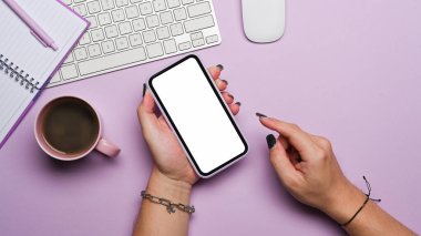 Mor arka planda akıllı telefon kullanan bir kadının el görüntüsü. Üst görünüm.