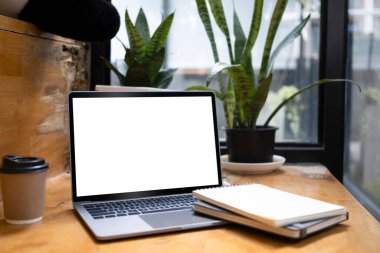 Laptop, defter, kahve fincanı ve ahşap tabağı olan rahat bir iş yeri.