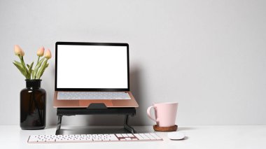 Bilgisayar laptopu, saksı ve kahve fincanı beyaz masada.