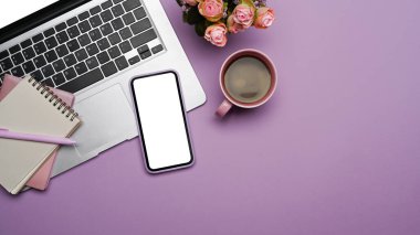 Mobile phone with blank screen, laptop computer and coffee cup on purple background.