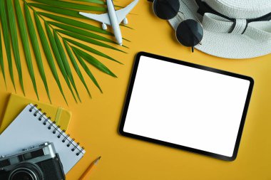 Düz tablet, boş ekran ve sarı arka planda gezgin aksesuarları vardı. Seyahat, yaz ve tatil konsepti.