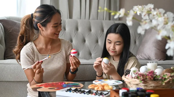 Smiling asian mother and her daughter enjoy painting Easter eggs together in living room. — Zdjęcie stockowe