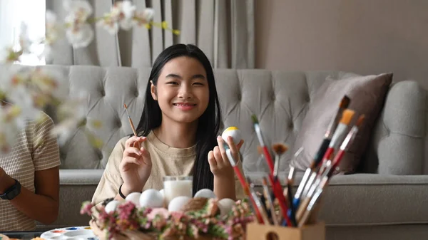 Happy girl painting Easter eggs with colors and brush at home. — 스톡 사진