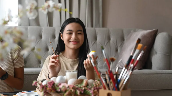 Happy girl painting Easter eggs with colors and brush at home. — Photo