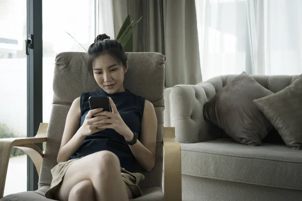 Millennial woman using smart phone while relaxing on armchair. — Foto Stock