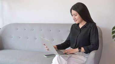 Çekici Asyalı kadın evdeki kanepede dinleniyor e-postaları kontrol ediyor, bilgisayarla çalışıyor..