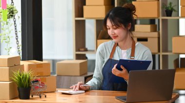 Çevrimiçi küçük işletme sahibi hesap makinesi kullanıyor ve teslimat için paket kutuları hazırlıyor