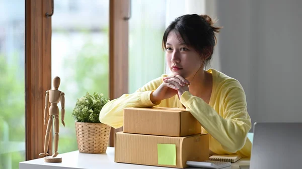 Zamyšlená obchodní žena prodávající on-line s lepenkových krabic sedí ve své domácí kanceláři — Stock fotografie