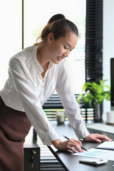 Asian female employee standing at her office desk and reading financial reports. — Stock Photo, Image