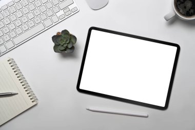 Üst görünüm dijital tablet, defter, kahve fincanı ve sulu bitki beyaz ofis masasında.