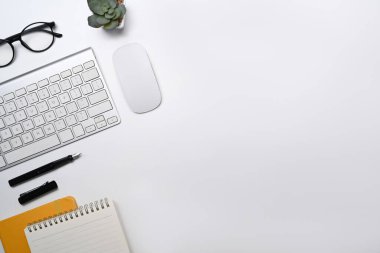 Kablosuz klavyesi, gözlüğü, defteri ve sulu bitkisi olan üst görünüm beyaz ofis masası