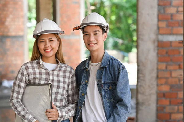 Twee civiele ingenieurs met een veiligheidshelm op op de bouwplaats en glimlachend naar de camera — Stockfoto