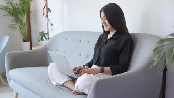 Szczęśliwy młody Azji kobieta relaks na kanapie i surfing internet, praca online z laptopa — Zdjęcie stockowe