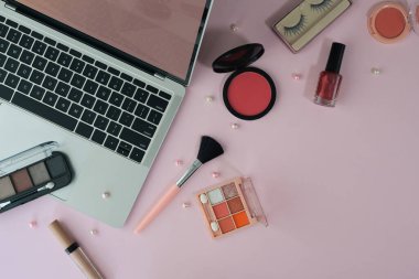 Top view feminine workspace with laptop and cosmetics on pink background