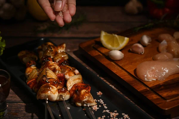 鶏や野菜の串焼きに塩や調味料を振りかける男の手 — ストック写真