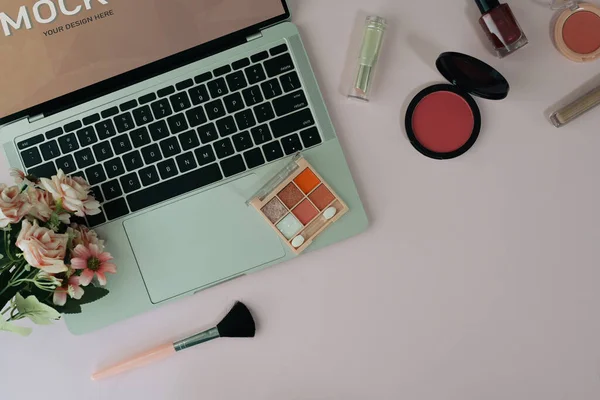 Lieu de travail féminin avec ordinateur portable, fleur et cosmétiques sur fond rose. Vue du dessus — Photo